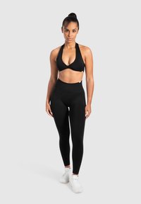 Zwarte sportieve crop top met halternek ontwerp, gecombineerd met hoge zwarte leggings. Model draagt witte sportschoenen.