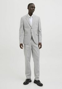 Costum în carouri gri deschis, cu croi slim, având o jachetă cu două butoane și pantaloni cu față dreaptă. Asortat cu o cămașă albă și pantofi negri.