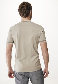 Maglietta beige chiaro a maniche corte con scollatura rotonda e polsini testurizzati. Il tessuto sembra liscio, indossata con jeans grigi.