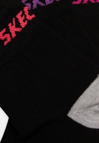 Sosete negre cu textură ribbată, având literele strălucitoare în roz și mov "SKEL" pe partea de sus. Include un accent alb aproape de vârf.