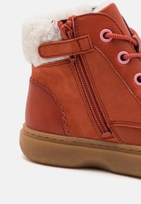 Stivale in pelle arancione con un morbido rivestimento crema, occhielli rosa e cerniera laterale. Presenta una suola in gomma texturizzata e dettagli ondulati.