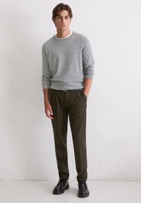 Szary sweter dzianinowy, dopasowane oliwkowe spodnie oraz czarne buty na sznurówki. Prosty design, okrągły dekolt, ściągacze na rękawach i w pasie.