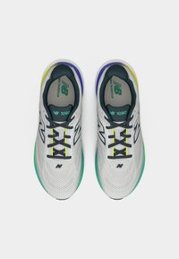 Ζευγάρι λευκών παπουτσιών για τρέξιμο New Balance 1080 με μαύρα κορδόνια και πράσινες, μπλε και κίτρινες λεπτομέρειες, σε άνω όψη πάνω σε λευκό φόντο.
