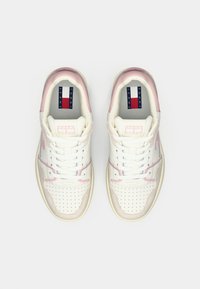 Een paar witte en roze Tommy Jeans sneakers met geperforeerde teentjes en veters, van bovenaf bekeken op een witte achtergrond.