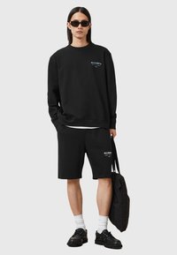 Ensemble sweatshirt noir et shorts avec logo sur la poitrine, assorti de chaussettes blanches et de chaussures noires. Comprend un sac noir. Tissu lisse et décontracté.