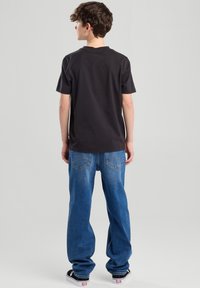 Musta puuvillapaita pyöreällä kaula-aukoilla, yhdistettynä sinisiin löysiin farkkuihin, joissa on takataskut ja hillityt ompelutiedot.