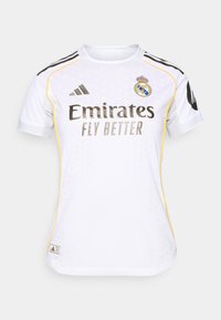 Maillot de football blanc avec des accents noirs et jaunes, caractérisé par un col rond, des manches courtes et le logo du Real Madrid sur la poitrine.