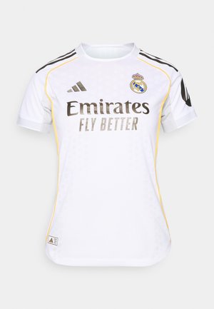 Witte voetbalshirt met zwarte en gele accenten, voorzien van een ronde hals, korte mouwen en het Real Madrid-logo op de borst.