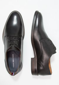 Bottines en cuir noir avec une finition lisse, un design à lacets et un talon en bois. Présentent un logo de marque subtil sur la semelle intérieure.