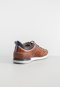 Brown leather sneaker with a textured finish, rounded shape, white rubber sole, navy textile accents, and lace-up design.