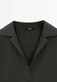 Chemise à col vert foncé avec un col en V et une texture lisse ; étiquette indiquant "Massimo Dutti" située à l'arrière du cou.