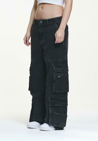 Black cargo pants made of denim with oversized pockets and a loose fit, featuring a button closure and contrasting stitching details.