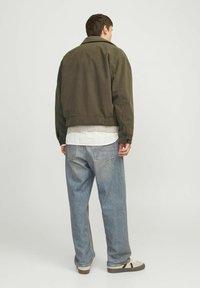 Oliivroheline korgiga jakk, millel on lõdvestunud lõige, koos helesiniste denimpükstega. Jakk on varustatud kraega ja nööbiga mansettidega.