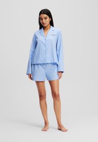 Set de pijamale de culoare albastru deschis, format dintr-o bluză cu mânecă lungă și nasturi și pantaloni scurți asortați, realizat dintr-un material neted și ușor.