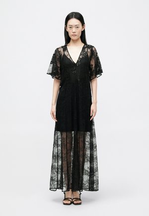 Svart spets maxikjol med V-ringning, korta utsvängda ärmar och ett genomskinligt överdrag; har ett blommönster och en figursydd midja.