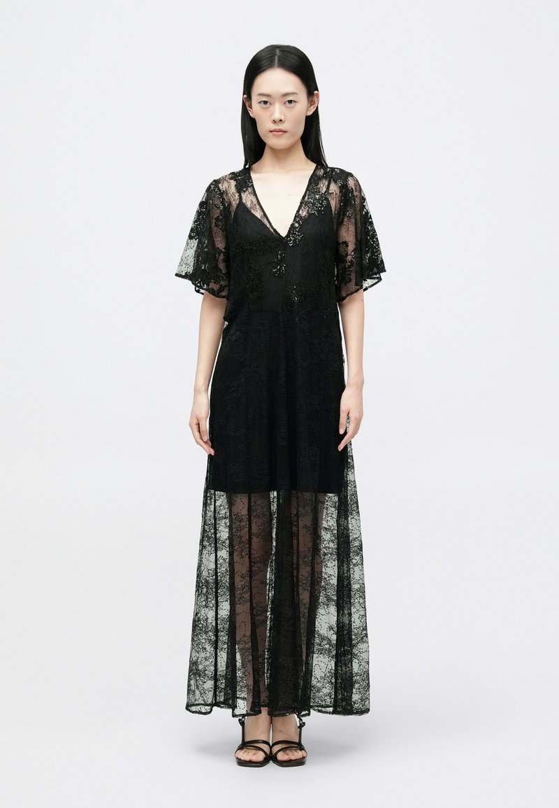 Juoda nėriniuota maksima su V formos iškirpte, trumpomis plačiomis rankovėmis ir permatomu uždengimu; turi gėlių raštą ir prigludusį liemenį.