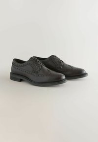 Chaussures brogue en cuir noir avec une finition texturée, présentant des perforations détaillées et un bout arrondi bas. Design classique à lacets.
