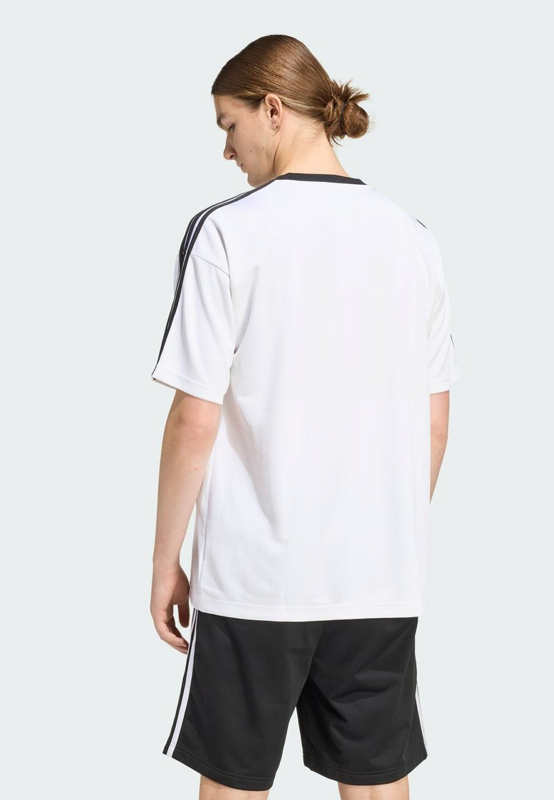 Camisa deportiva blanca con detalles y rayas negras. Mangas cortas y escote redondeado. Combinada con pantalones cortos negros, hechos de tejido transpirable.