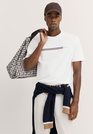 White T-shirt with horizontal maroon and blue stripes, paired with navy sweater tied at the waist and a patterned tote bag. Brown cap.