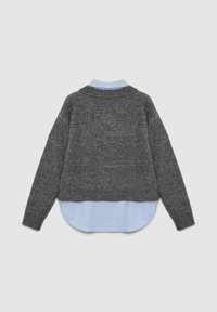 Grauer Strickpullover mit hohem Kragen, verkürztem Design und langen Ärmeln, über einem hellblauen Hemd mit abgerundetem Saum getragen.