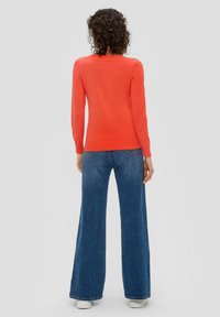 Rode trui met lange mouwen en geribbelde manchetten, gecombineerd met wijde blauwe denim jeans. De outfit heeft een casual, ontspannen pasvorm.