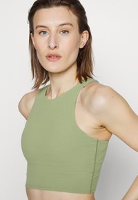 Top cropped verde claro feito de um tecido suave. Apresenta um decote alto e um design sem mangas, com costura visível ao longo das bordas.