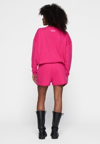 Conjunto de sudadera y pantalones cortos de color rosa brillante, hecho de una tela suave. La sudadera presenta hombros caídos, mientras que los pantalones cortos tienen un corte holgado. Botas negras hasta la rodilla completan el look.