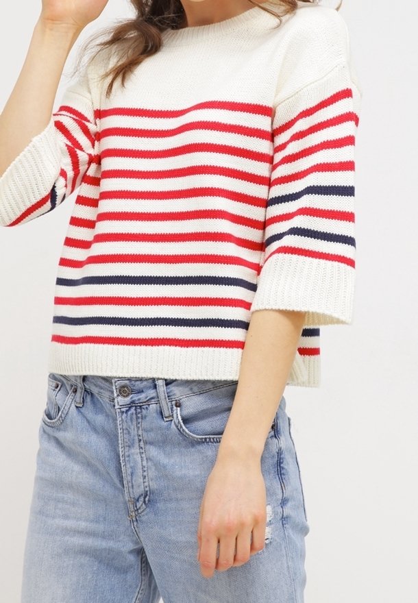Suéter a rayas en crema, rojo y azul marino, con un cuello redondo y mangas cortas y anchas. Combinado con jeans desgastados de color azul claro.