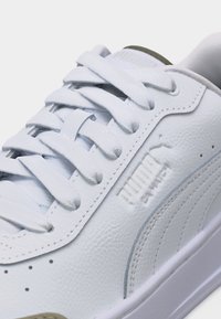 Κοντινό πλάνο λευκού αθλητικού παπουτσιού Puma Clyde με υφή δέρματος, ραμμένες λεπτομέρειες και λευκά κορδόνια δεμένα σε διασταυρούμενο μοτίβο.