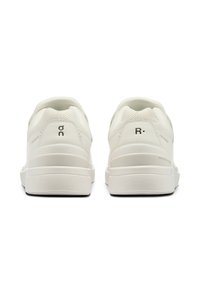 Le scarpe da ginnastica bianche presentano una tomaia in rete texturizzata, un design elegante, un collare imbottito e un marchio distintivo sul tallone e sul lato.