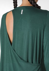 Top verde a maniche lunghe con grande scollatura sul retro e piccolo etichetta a collo. Tessuto morbido con una superficie liscia.