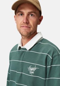 Grün gestreiftes Poloshirt mit einem weißen Kragen und gesticktem "Honestly Rules"-Logo. Weicher Stoff, lässige Passform.