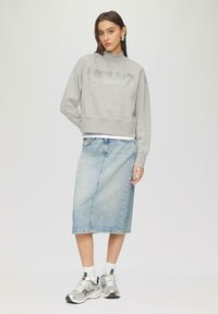 Grijs cropped sweatshirt met "HELLO" in glanzende details, gecombineerd met een lichtblauwe denim midi-rok. Geaccessoireerd met zilveren sneakers en witte sokken.