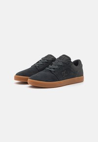 Black suede sneakers with a rubber gum sole, rounded toe, flat laces, and branding on the side. They feature a minimalist design.