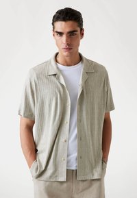 Short-sleeve, light gray textured shirt with a collar, button front, and subtle pattern; worn over a white crew-neck t-shirt.