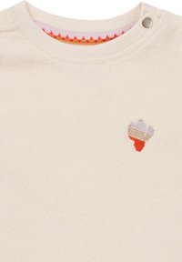 Beige Fleece-Shirt mit langen Ärmeln, das ein kleines, mehrfarbiges gesticktes Design auf der Brust und einen gemusterten inneren Kragen mit Druckknopfverschluss aufweist.