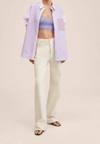 Gestreiftes, übergroßes Lavendelhirt mit kurzen Ärmeln, kombiniert mit hellbeigen, weit geschnittenen Hosen und schwarzen Flip-Flops. Lässiges Outfit.