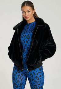Chaqueta bomber de piel sintética negra con cierre de cremallera y cuello ancho, superpuesta a un body de estampado de leopardo azul con un cuello alto.