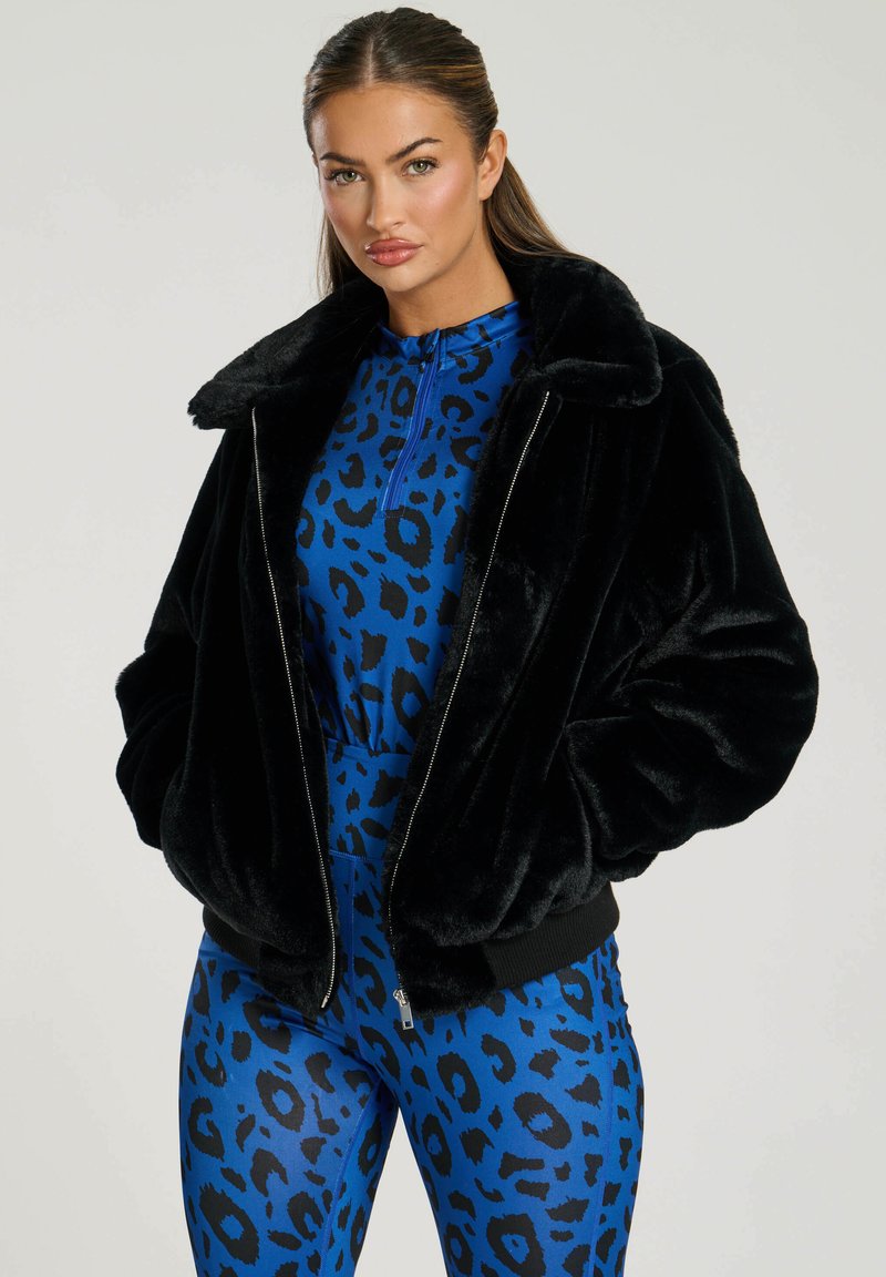 Chaqueta bomber de piel sintética negra con cierre de cremallera y cuello ancho, superpuesta a un body de estampado de leopardo azul con un cuello alto.