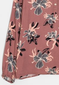Langärmlige, rosafarbene Bluse mit einem floralem Muster in Schwarz und Hellrosa. Knopfverschluss am Halsausschnitt, geraffte elastische Bündchen. Weicher Stoff.