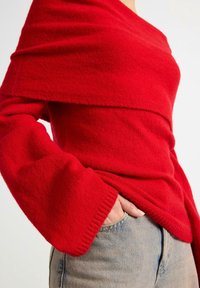 Rød uldtrøje med indpakningsdesign, der har brede ærmer og ribbede manchetter, parret med lyseblå denimjeans.