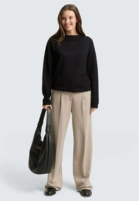 Sweat-shirt noir à large encolure, pantalon beige taille haute, et grand sac à bandoulière en cuir noir, avec une texture lisse et une coupe décontractée.