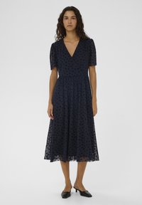 Tengerészkék, térdig érő ruha rövid pödrött ujjakkal, V-nyakkivágással és virágmintával. Könnyű, texturált anyagból készült, lebegő szoknyával.