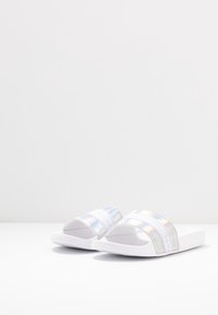 Infradito bianchi con due fascia iridescenti e suola piatta. Logo stampato sulle fascette; texture liscia e forma arrotondata.