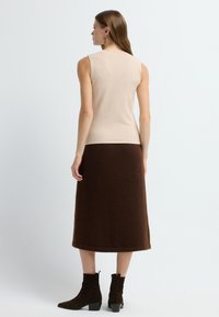 Beige mouwloze top van zachte stof, gecombineerd met een knielange, donkerbruine, pluizige rok en bruine enkellaarzen met een blokhak.