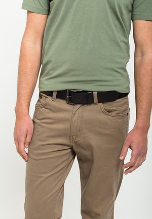 Brune bukser med lige pasform, parret med en ensfarvet grøn T-shirt. Et sort bælte med en rektangulær spænde fuldender outfittet.
