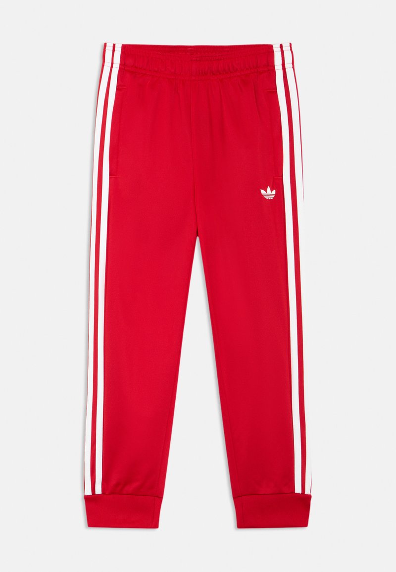 Raudonos sportinės kelnės su baltomis šoninėmis juostomis, elastine juosmens dalimi ir ribotais rankogaliais. Medžiaga atrodo lygi su siuvinėta logo.