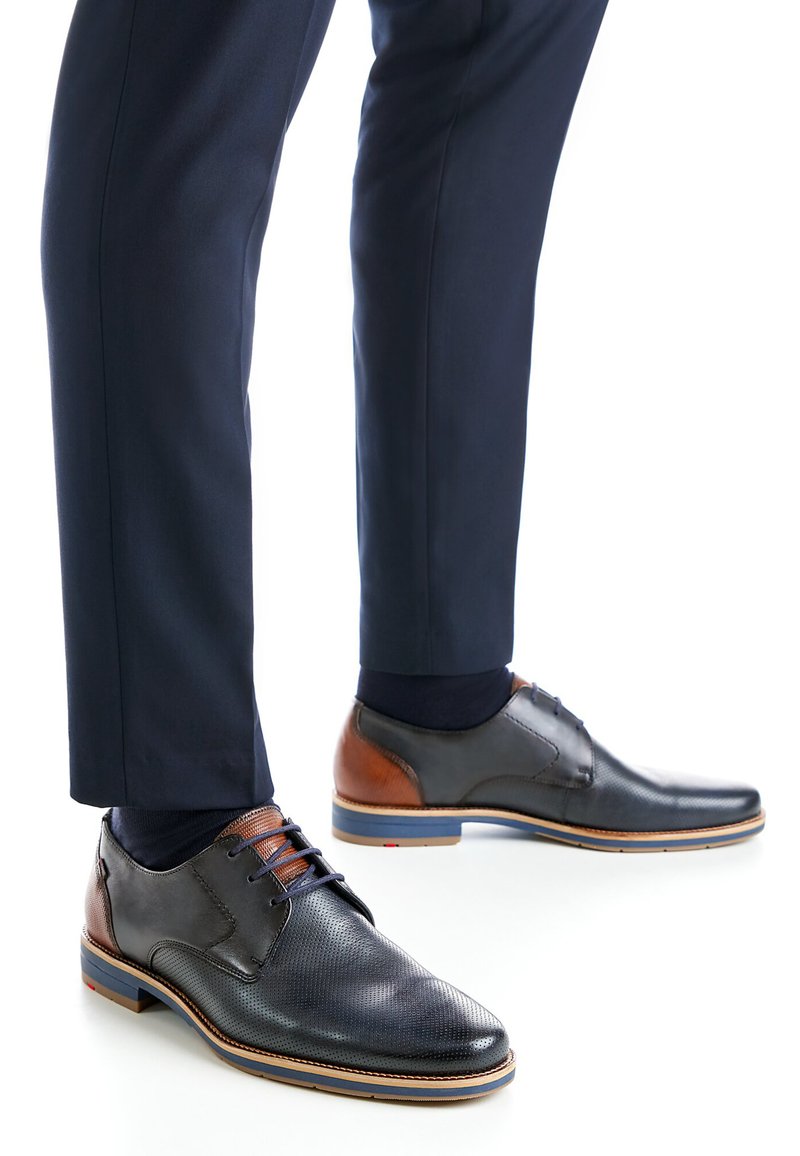 Musta nahkainen juhlakenkä, jossa on teksturoidun pinnan ja ruskeat yksityiskohdat, nauhat ja kontrastinen sininen viimeistely pohjassa.