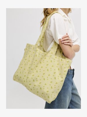 Personne portant une chemise blanche à manches courtes et un jean bleu, portant un grand sac cabas jaune avec de petits motifs floraux verts.