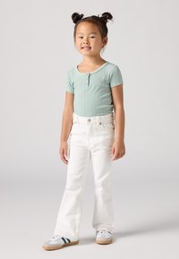 Body vert clair à manches courtes à rayures, jean flare blanc et baskets grises avec des rayures vertes, avec un détail de bouton en haut.